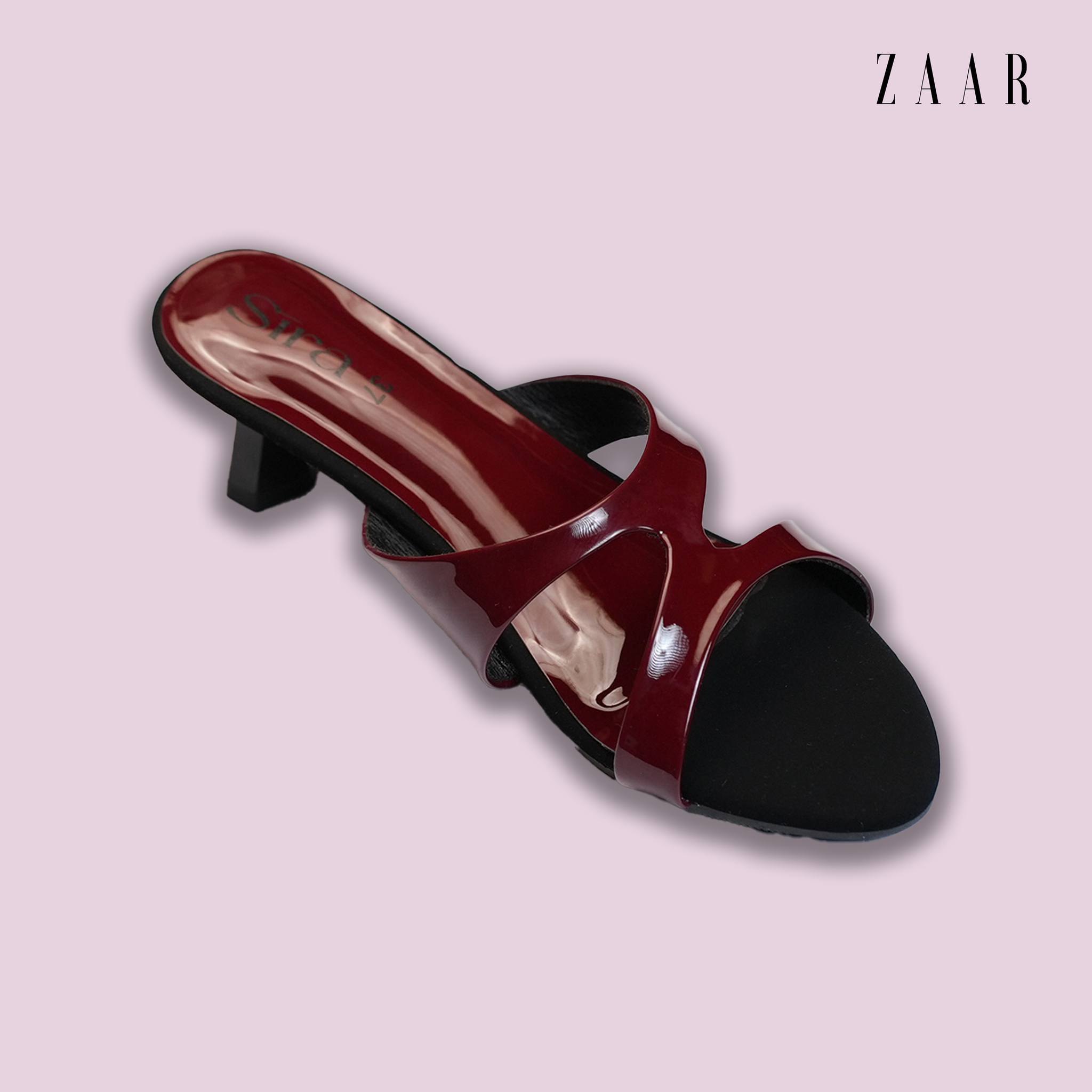 A Sira burgundy patent kitten-heel mule on a pale pink ground.